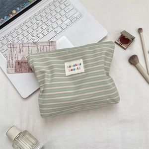 Flat lay of green and pink striped cosmetic bag with a chic logo on a desk background