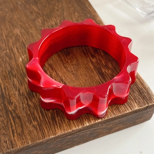 Detail of red marble texture resin bangle with unique wavy gear edges on wood