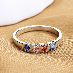Macro shot of silver ring with four colorful round zircons on golden silk fabric