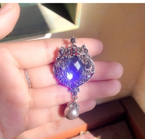 Detailed view of a vintage baroque brooch with a blue gemstone and grey pearl pendant