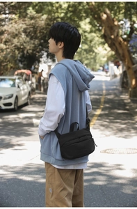 Close-up of black nylon crossbody bag worn on person in outdoor street setting