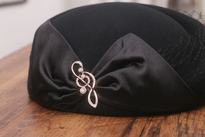 Close-up of wool beret featuring a satin bow, musical note brooch and black birdcage veil