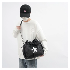 Close-up of black nylon crossbody bag with white star logo worn by model in white hoodie
