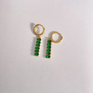 Detail of gold-plated tassel earrings featuring five green oval zircon gemstones on leather