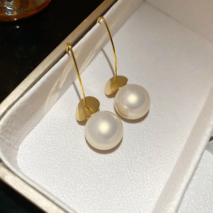 Detailed close-up of golden metal ear hook earrings with round white pearl drop