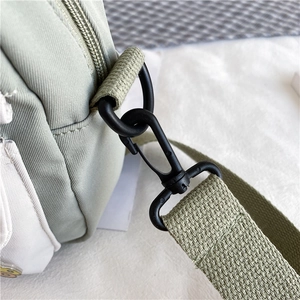 Détail de la sangle en toile avec crochet en métal noir mat sur le sac bandoulière vert