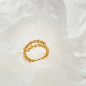 Detail of 18K gold beaded double-layer wave ring on white textured fabric background