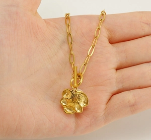 Detail of hand holding golden titanium pearl necklace with flower pendant and OT clasp