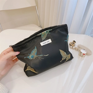 Detailed view of colorful butterfly embroidery on a black satin cosmetic bag with zipper