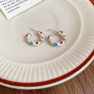 Detail of white enamel C-shaped earrings with colorful dots on a ceramic plate