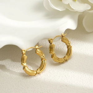 18k gold plated stainless steel bamboo hoop earrings hanging on white ceramic vase