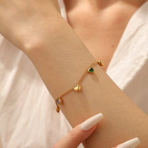 Close-up of golden bracelet with heart pendants and green and purple zircon stones on wrist