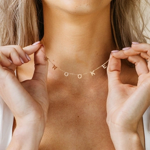 Close-up of a custom gold letter necklace spelling BROOKE worn by a female model
