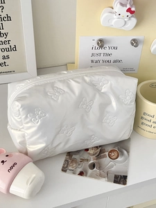 Detail of cream quilted makeup bag with embossed bow patterns and pearl charm