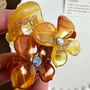 Amber acetate floral hair claw clip with crystal rhinestones held in hand