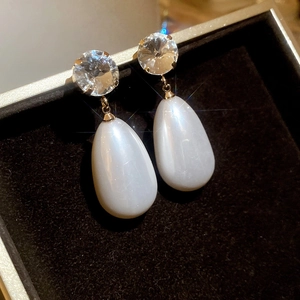 Detailed close-up of sparkling zircon and teardrop pearl earrings in gold finish