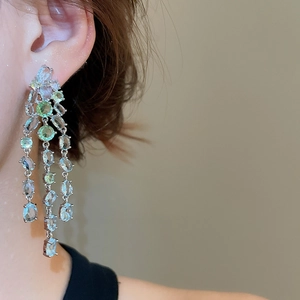 Nahaufnahme eleganter Silber-Ohrringe mit grünen Kristallen und Quasten an einem Model