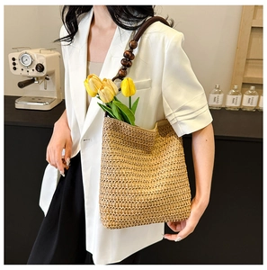 Detail of hand-woven straw beach bag featuring dark wooden bead handles and floral accents