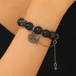 Dark green beaded bracelet with vintage silver dragon charm and bell on model's wrist