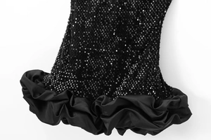 Détail des paillettes noires et de l'ourlet en satin plissé sur une robe de cocktail
