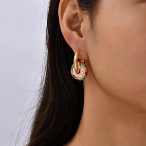 Detailaufnahme eines goldenen Creolen-Ohrrings mit roter Emaille-Blumenperle am Modell