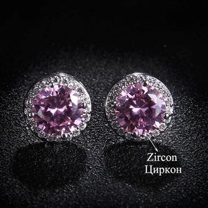 Macro shot of pink round zircon earrings with halo stones on a black reflective background