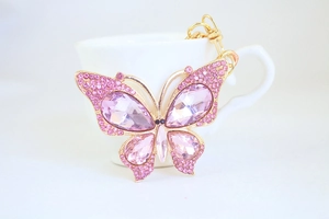 Macro shot of pink crystal butterfly keychain with gold plating in a white teacup