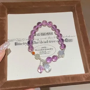 Macro detail of amethyst snake bead bracelet with silver clover pendant and letter charm
