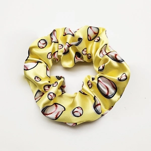 Detailed macro view of a yellow satin hair scrunchie with a vivid baseball print pattern