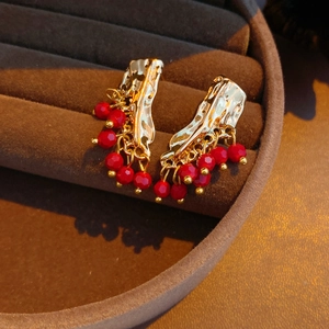 Dettaglio di orecchini vintage dorati con nappe in occhio di tigre rosso su vassoio marrone