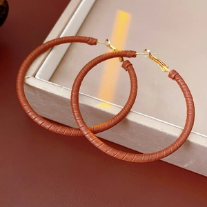 Detail of brown leather textured hoop earrings with gold-toned metal clasps on a display box