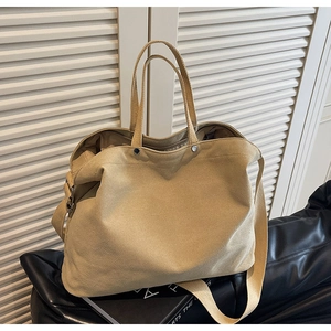 Detail of khaki canvas tote bag with dual handles and long shoulder strap on black stand