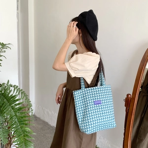 Detail view of large blue checkered canvas tote bag worn by a model in a casual setting