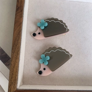 Detailed view of two cute grey and pink hedgehog hair clips on a soft beige velvet tray