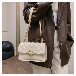 Quilted beige shoulder bag with gold metal buckle shown on a model in leather blazer