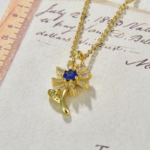 Macro shot of gold sunflower pendant with blue center stone and white petals on vintage paper