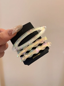 Close-up of three iridescent cream acetate hair clips on a black display card