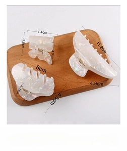 Detailed comparison of white pearlescent hair claws in three sizes on a wooden surface