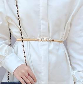 Detail of gold elastic waist chain with pearl buckle paired with a white shirt