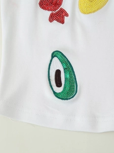 Macro shot of white knit fabric featuring avocado sequin embroidery and colorful patches