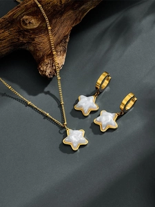 Detail of gold star pendant necklace and matching earrings on a textured background