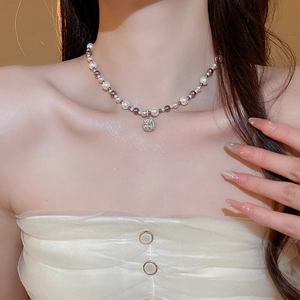 Detail of beaded pearl necklace with purple accents and a square zircon pendant on neck