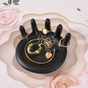 Nordic resin hand-shaped jewelry tray holding gold rings and necklaces on floral backdrop