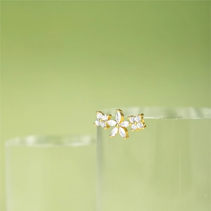 Macro detail of gold flower ear stud with diamonds and fringe on green background