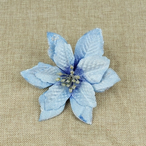 Blue artificial Christmas flower with silver glitter edges on beige linen background