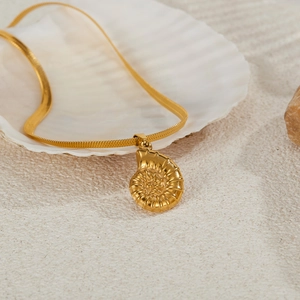 Elegant gold nautilus shell pendant necklace with a sleek snake chain on a sandy background