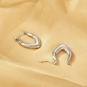Detail shot of silver geometric earrings with spiral texture on gold satin background