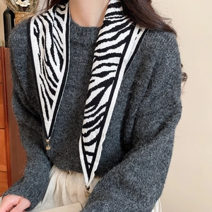 Detail of knit zebra pattern shawl with small metal bell pendant on a soft mohair sweater