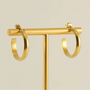 Close-up of golden C-shaped hoop earrings with brushed metal finish on a display stand