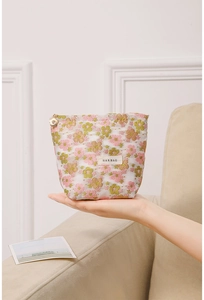 Detailed view of floral mesh makeup bag with golden flower zipper and brand label